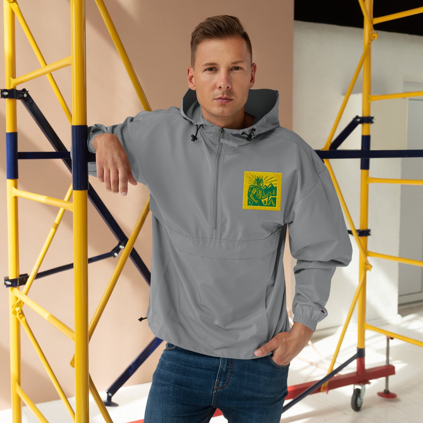 Man wearing a gray jacket with a green logo in front of yellow scaffolding.