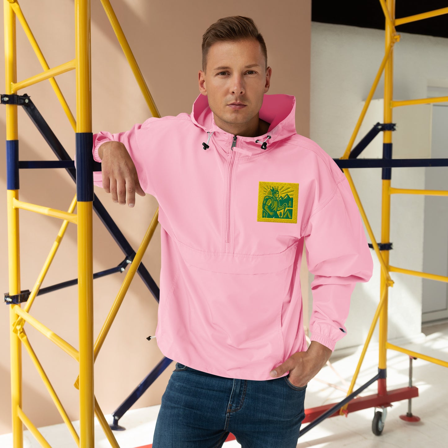 Man wearing a pink hoodie with a logo, standing in front of yellow scaffolding.