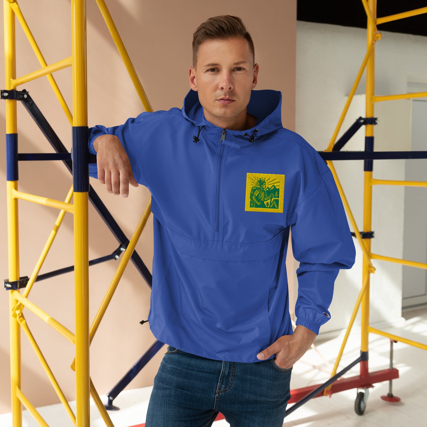 Man wearing a blue jacket with a yellow logo in an indoor setting with scaffolding.