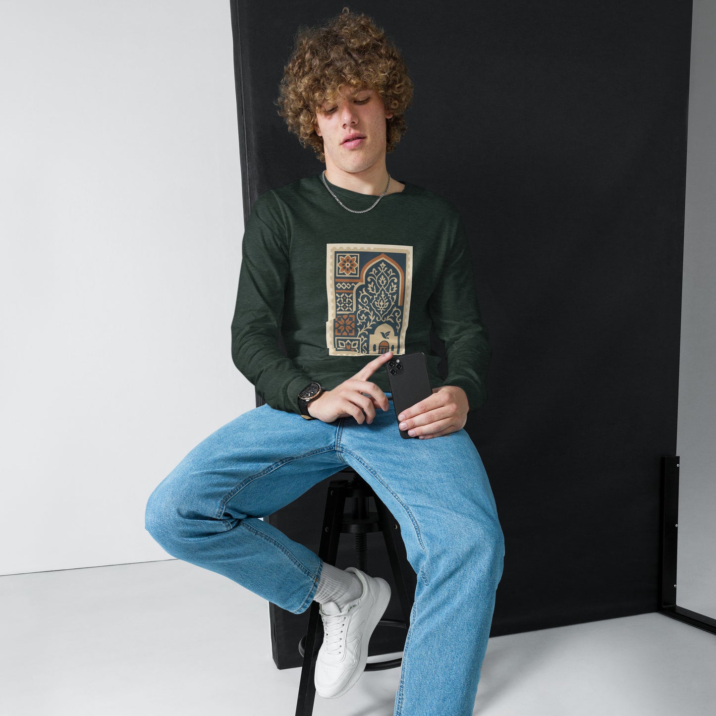 Person wearing a green long-sleeve shirt with a graphic design, sitting on a black stool against a white background.