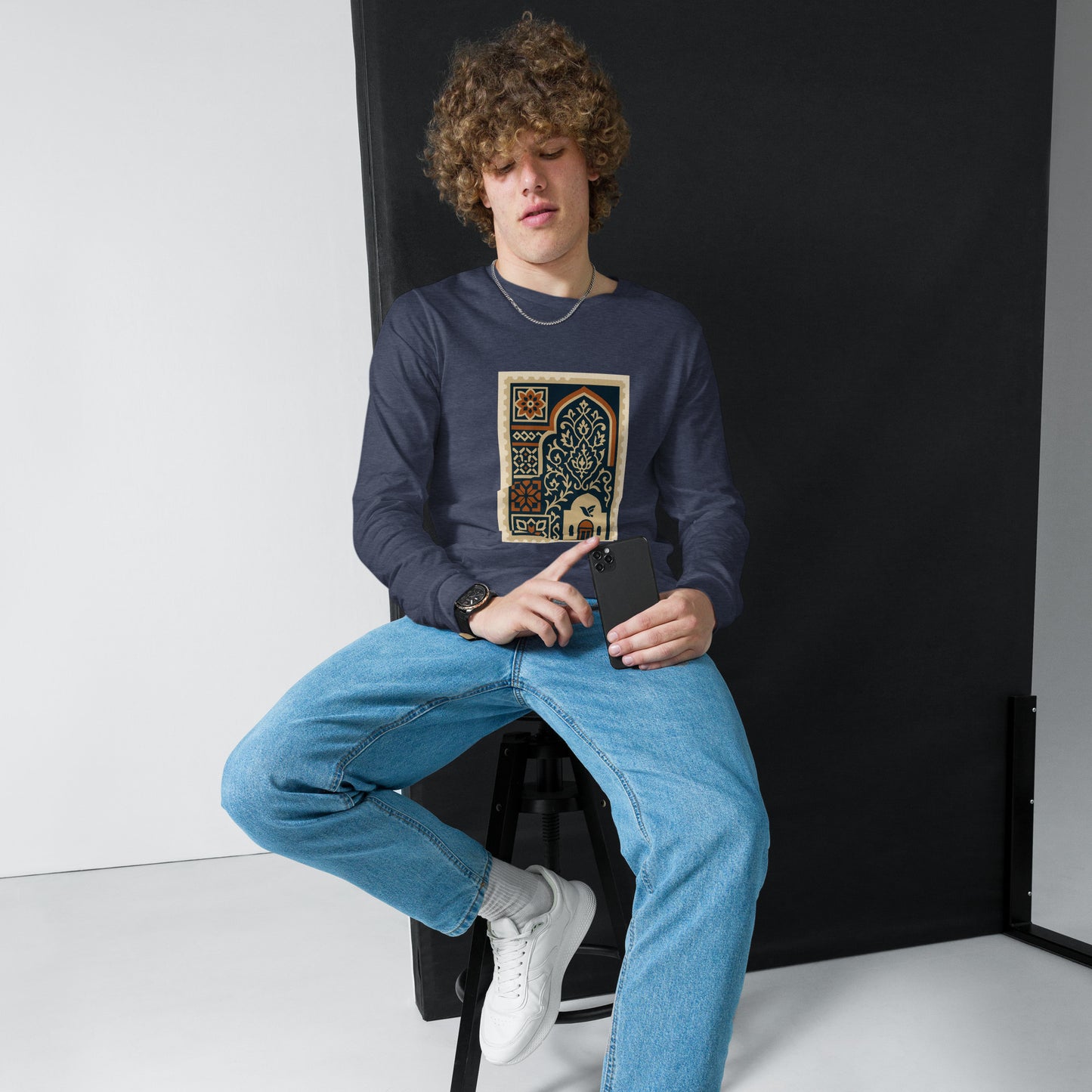 Person wearing a dark blue sweatshirt with a graphic design, sitting on a black stool against a white background.