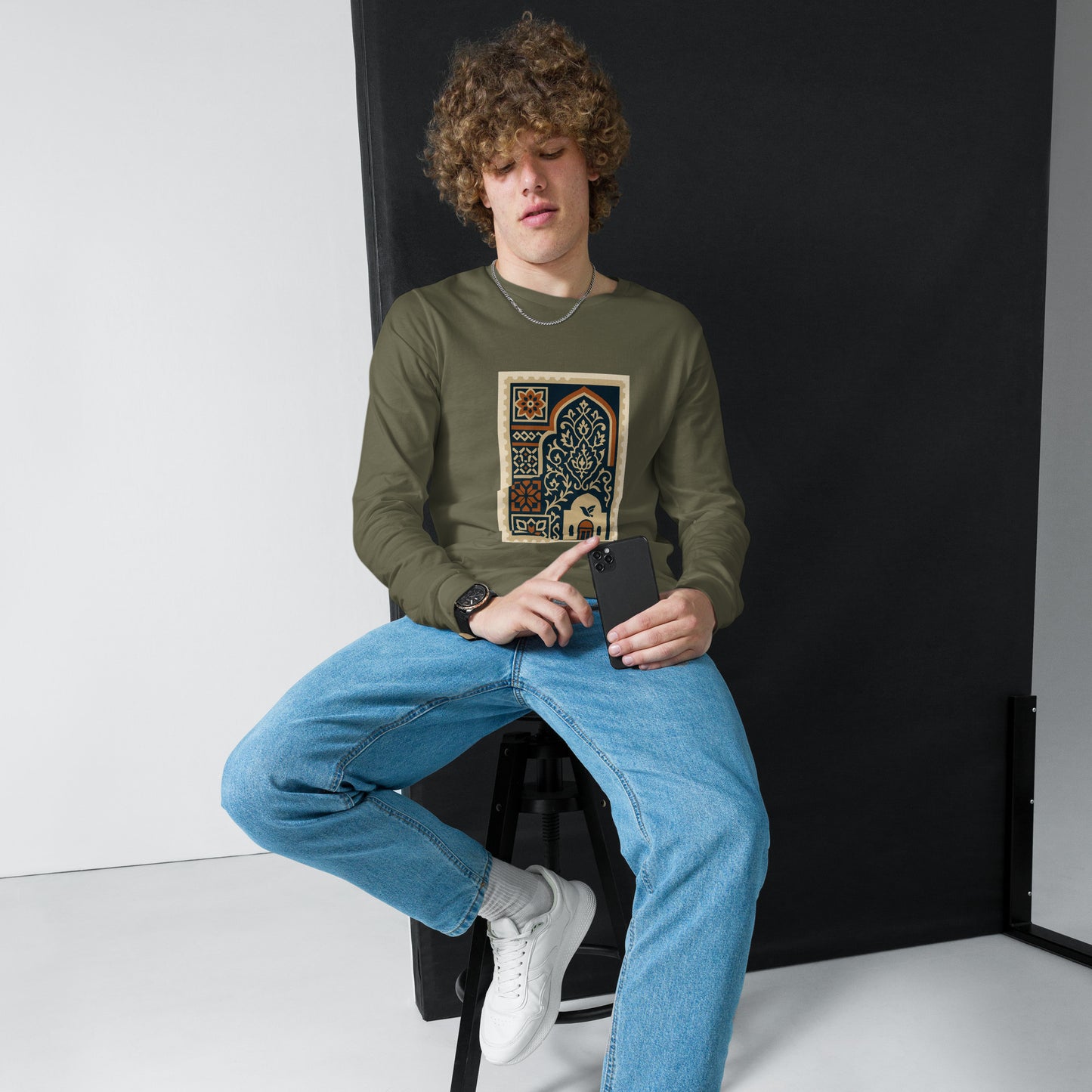Person wearing a green sweatshirt with a graphic design, sitting on a black stool against a white background.