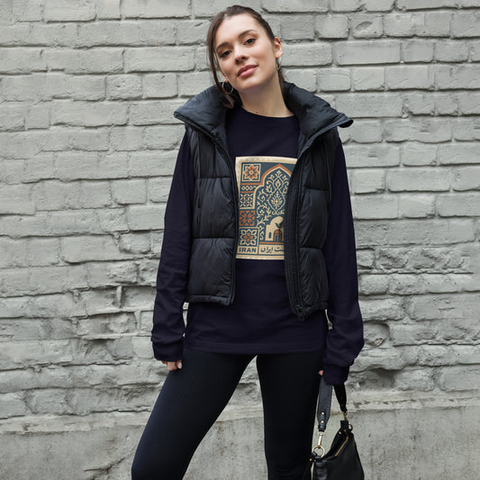 Woman wearing a dark jacket and black pants with a graphic t-shirt against a brick wall.