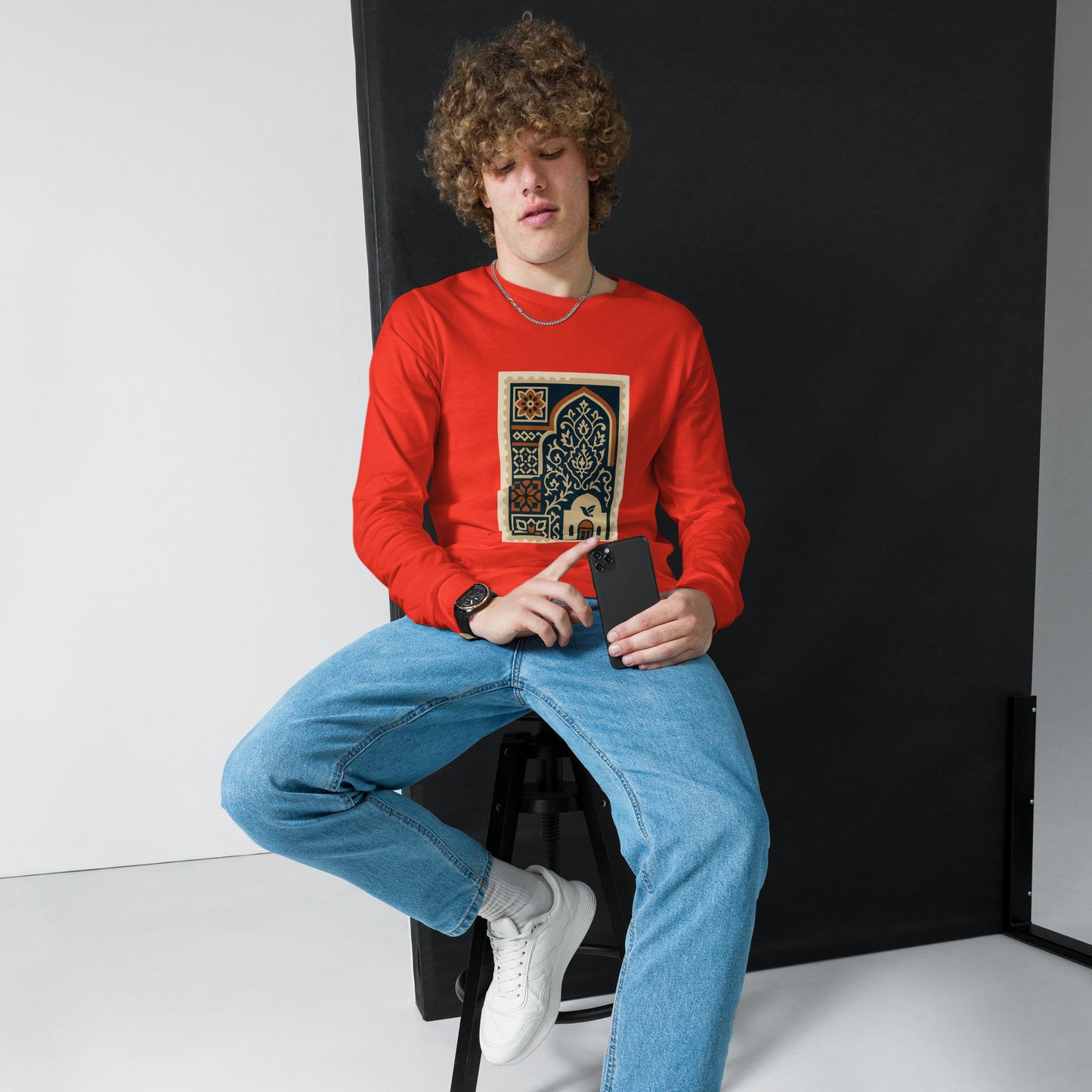 Person wearing a red sweatshirt with a graphic design, sitting against a black backdrop.