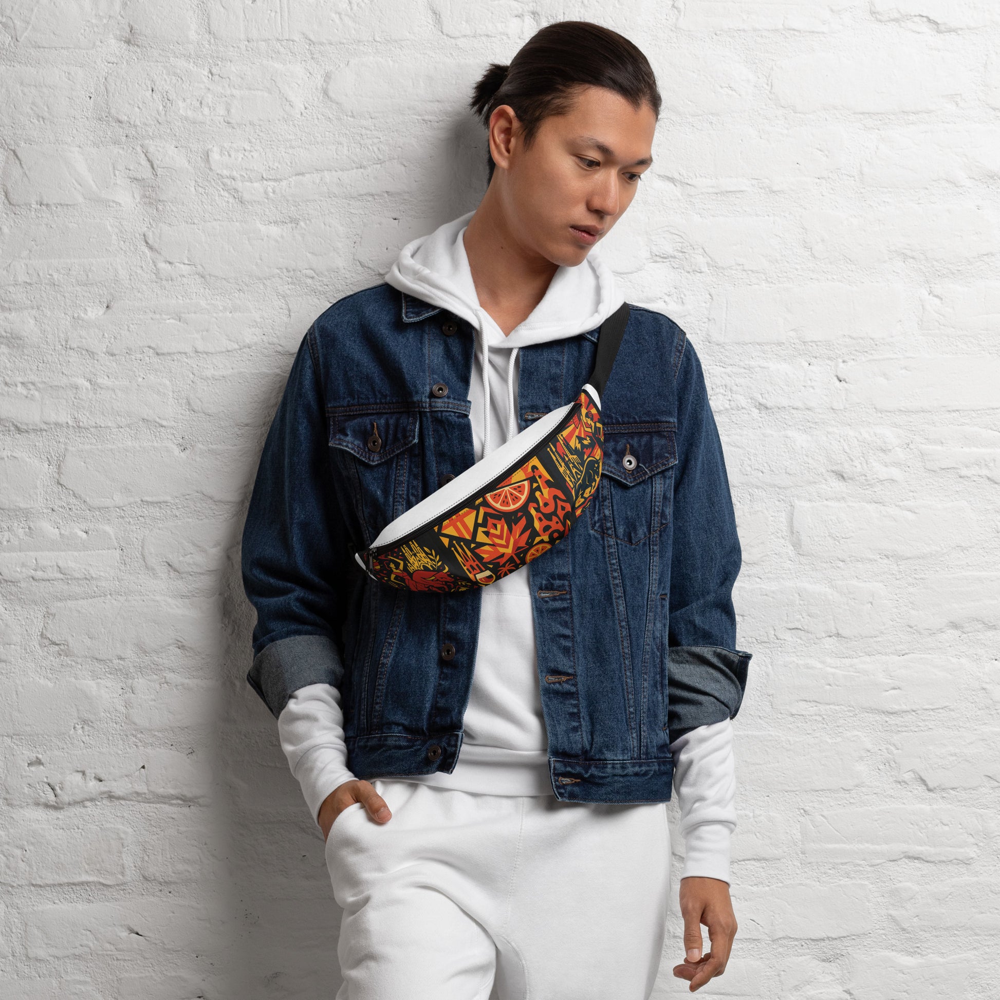 Person wearing a denim jacket and white hoodie with a colorful bag, standing against a white brick wall.