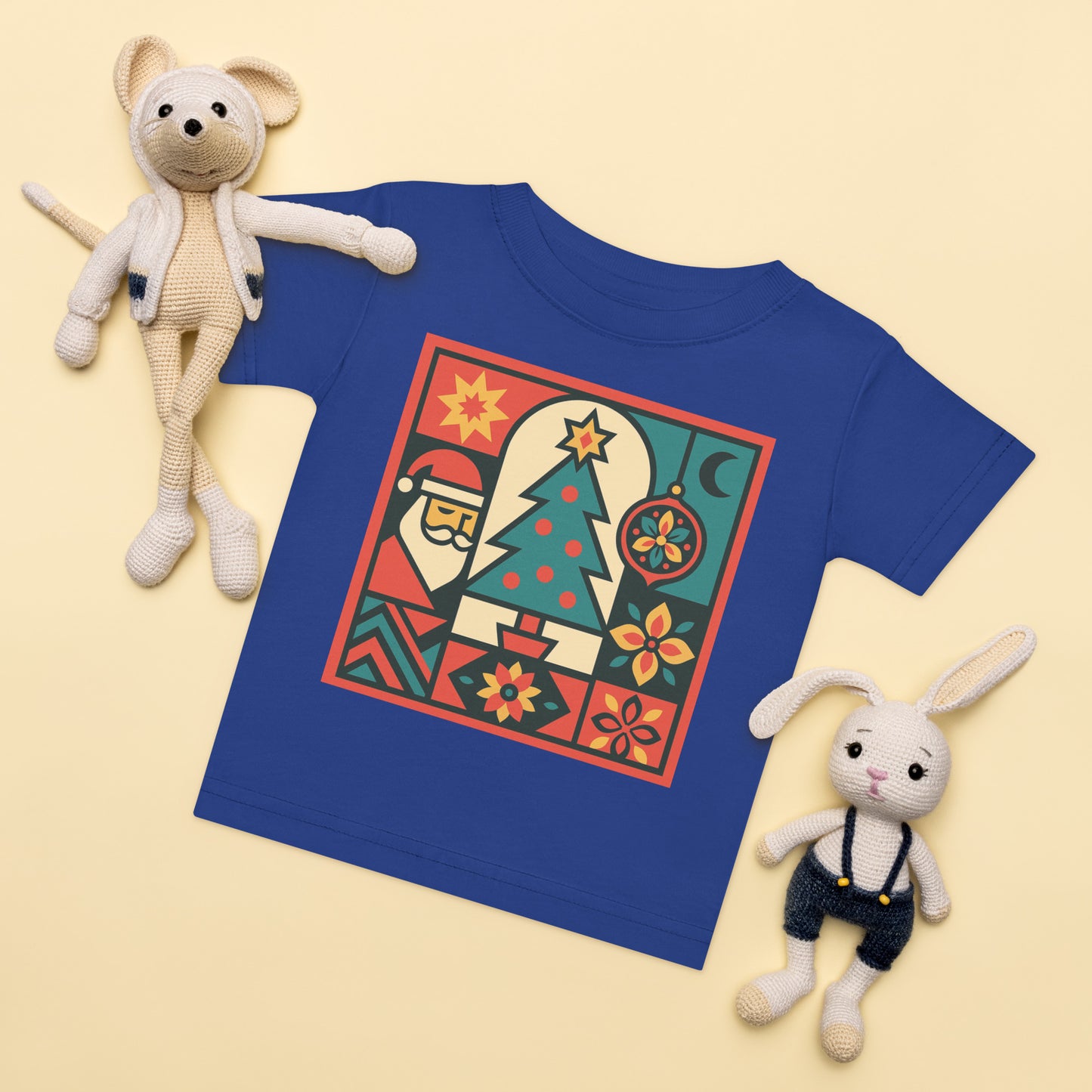 Blue t-shirt with festive design surrounded by two plush toys on a beige background