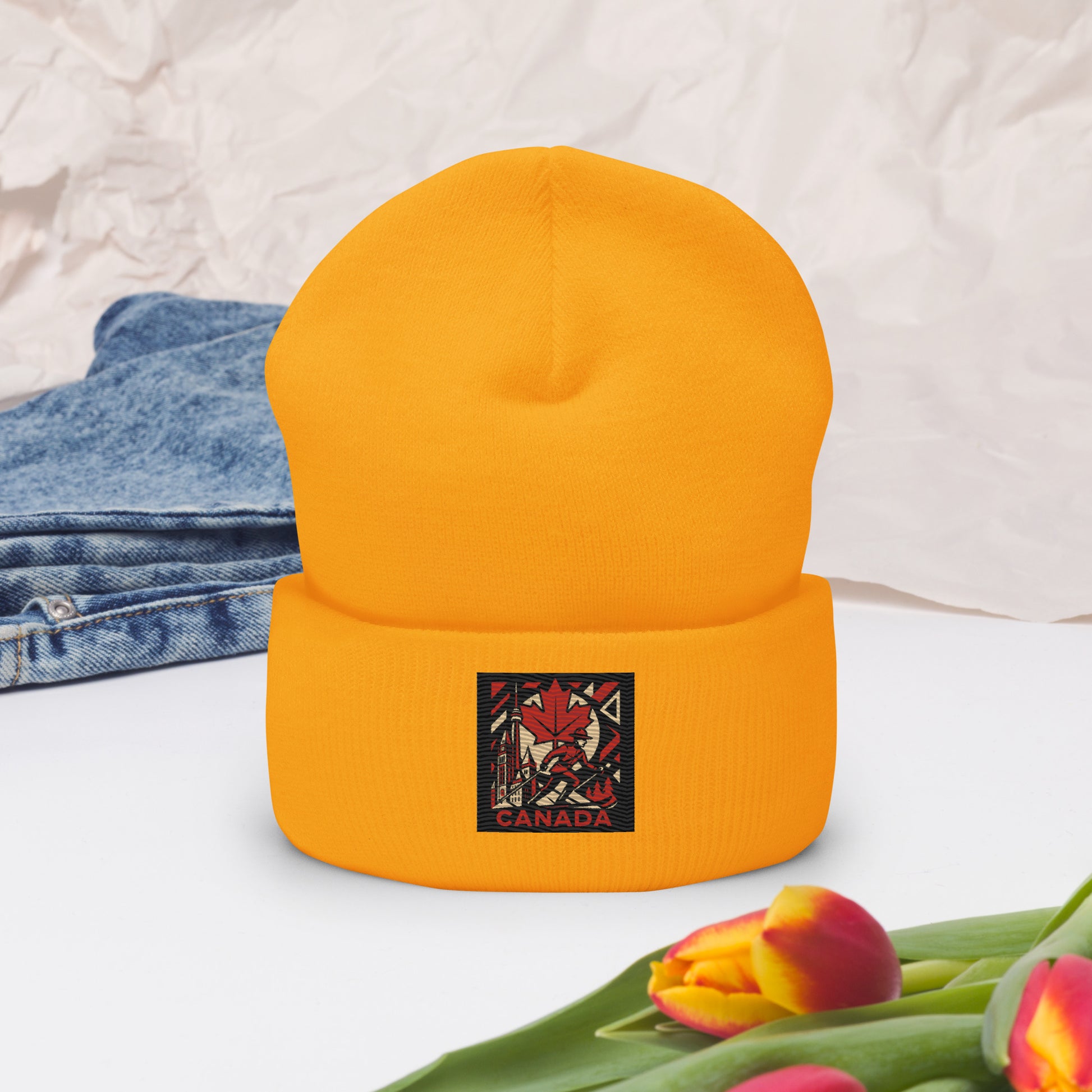 Yellow beanie with a 'Canada' logo on a white surface with jeans and tulips.