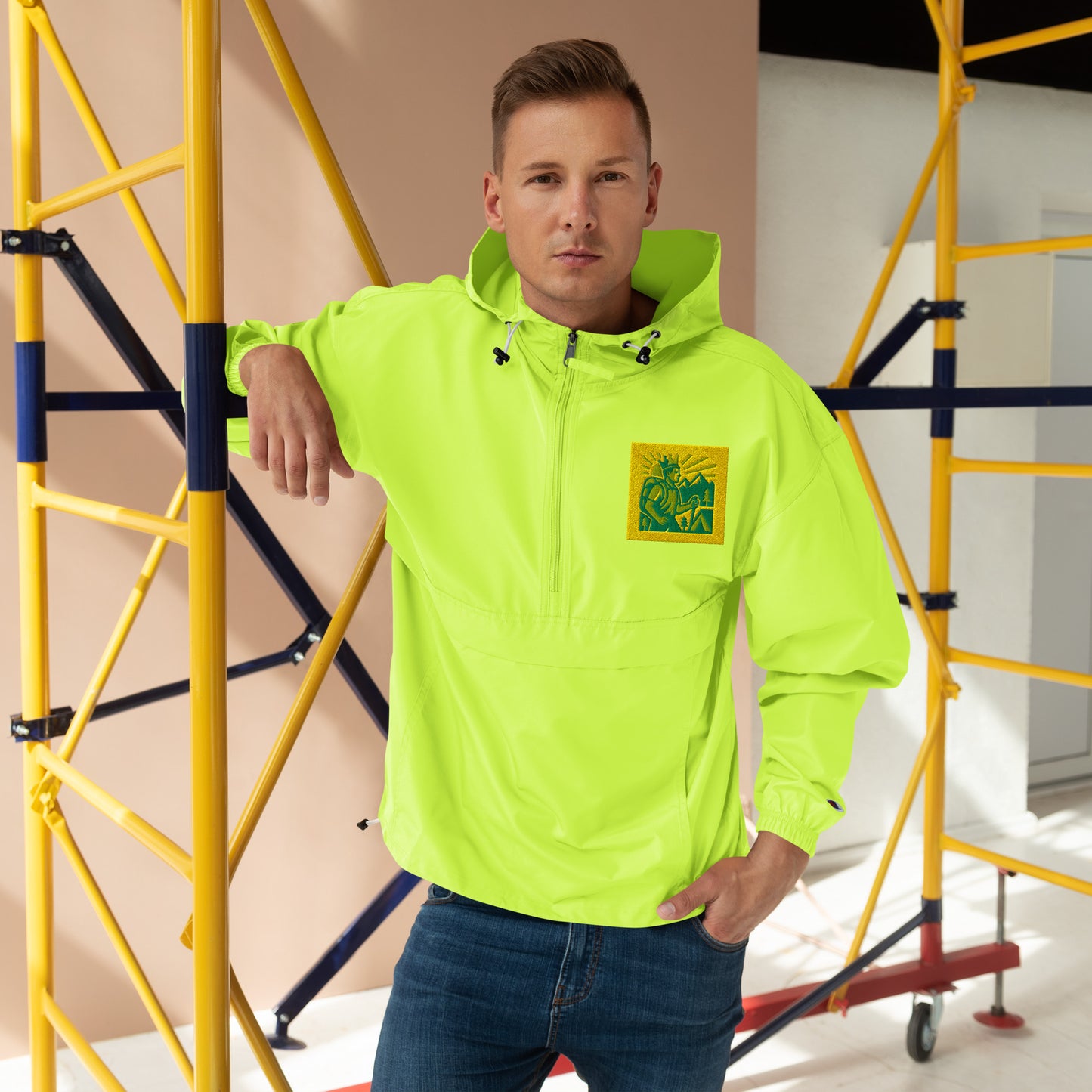 Man wearing a bright yellow jacket with a logo, standing in front of scaffolding.