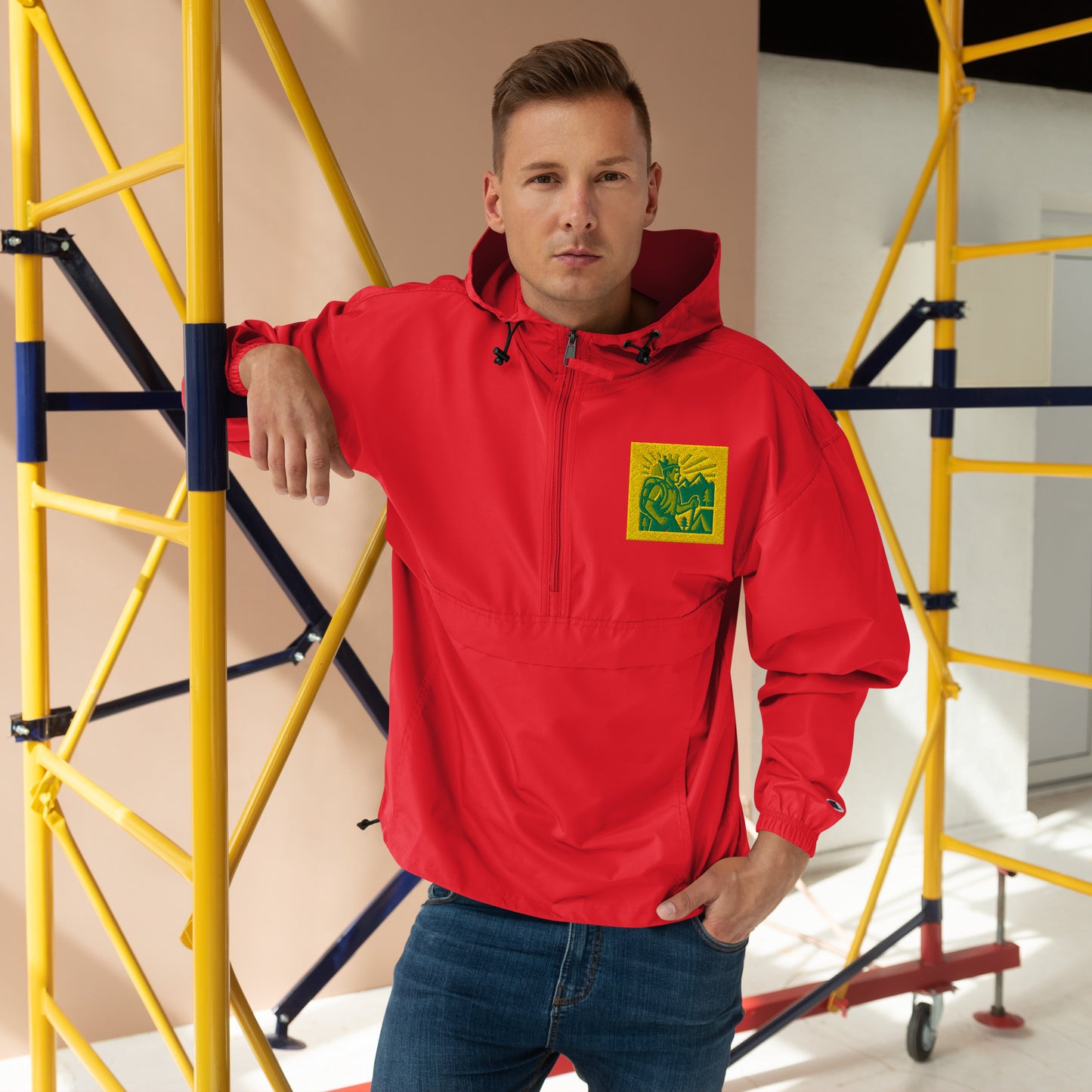 Man wearing a red jacket with a logo, standing in front of yellow scaffolding.