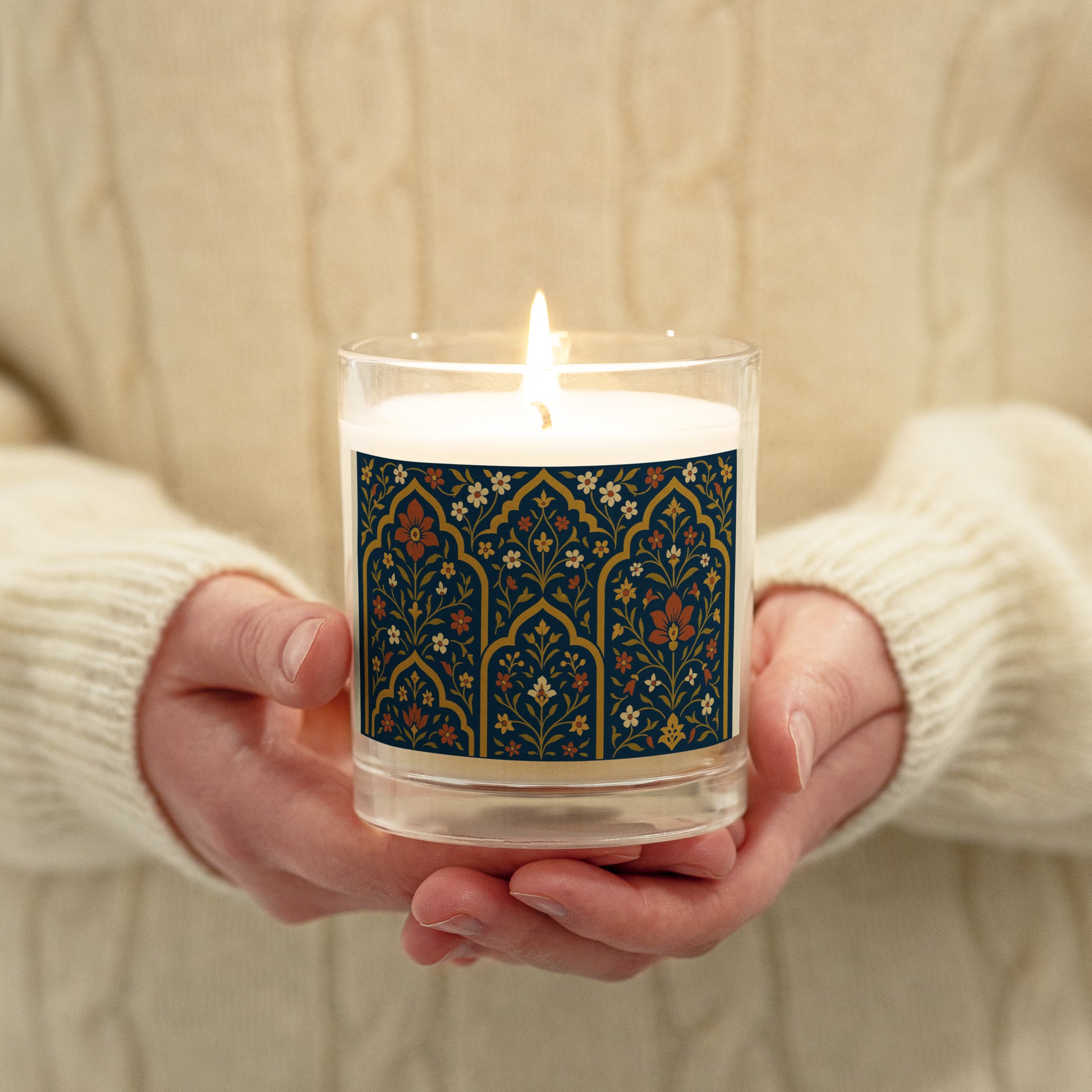 Candle with a decorative label held by hands against a neutral background