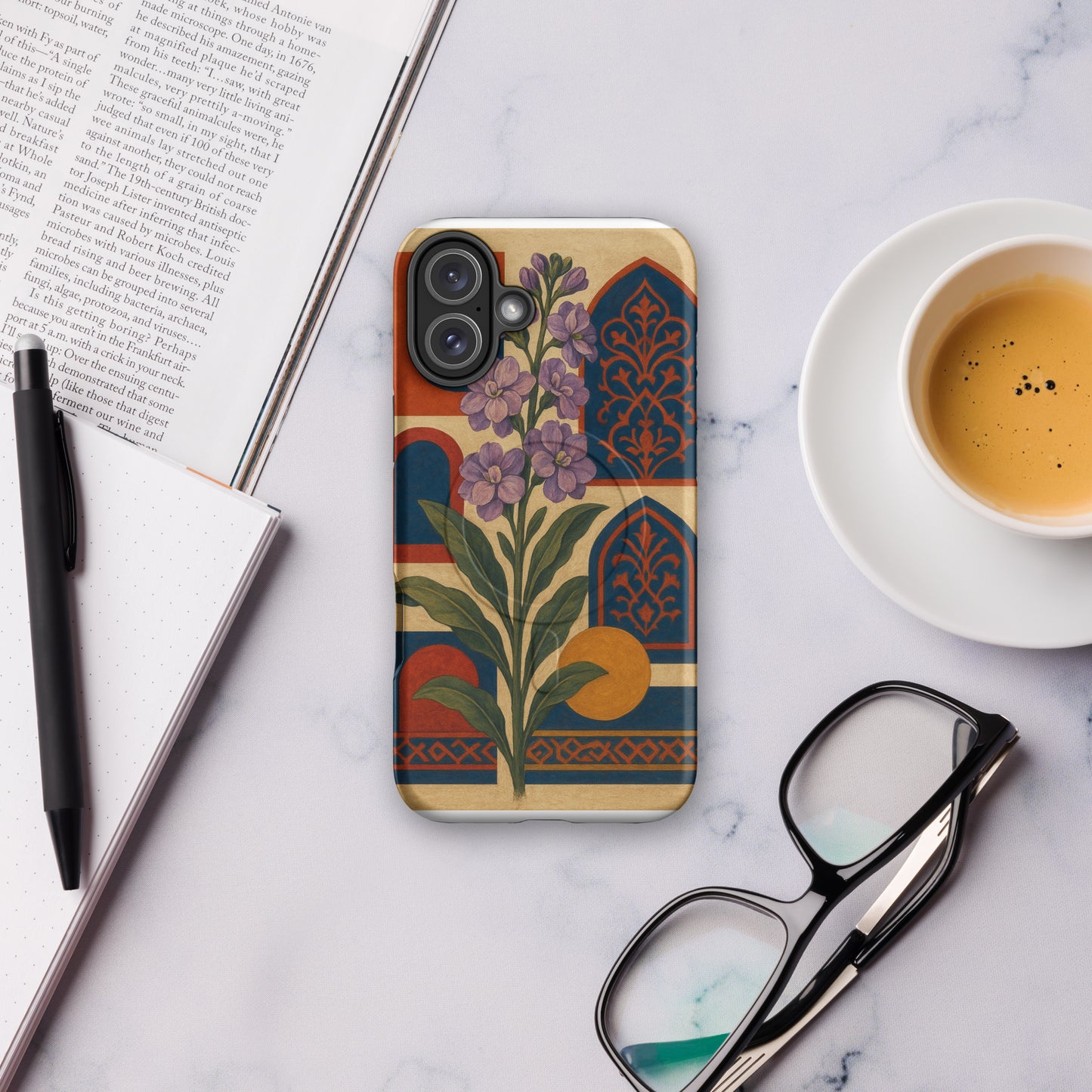Phone case with floral design on a marble surface with a book, pen, and coffee cup.