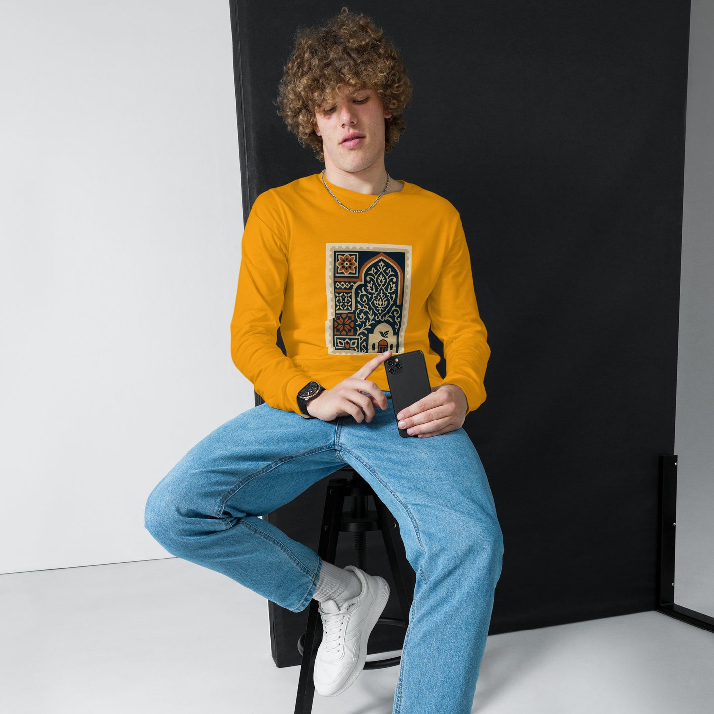 Person wearing a yellow sweatshirt with a graphic design, sitting against a black backdrop.