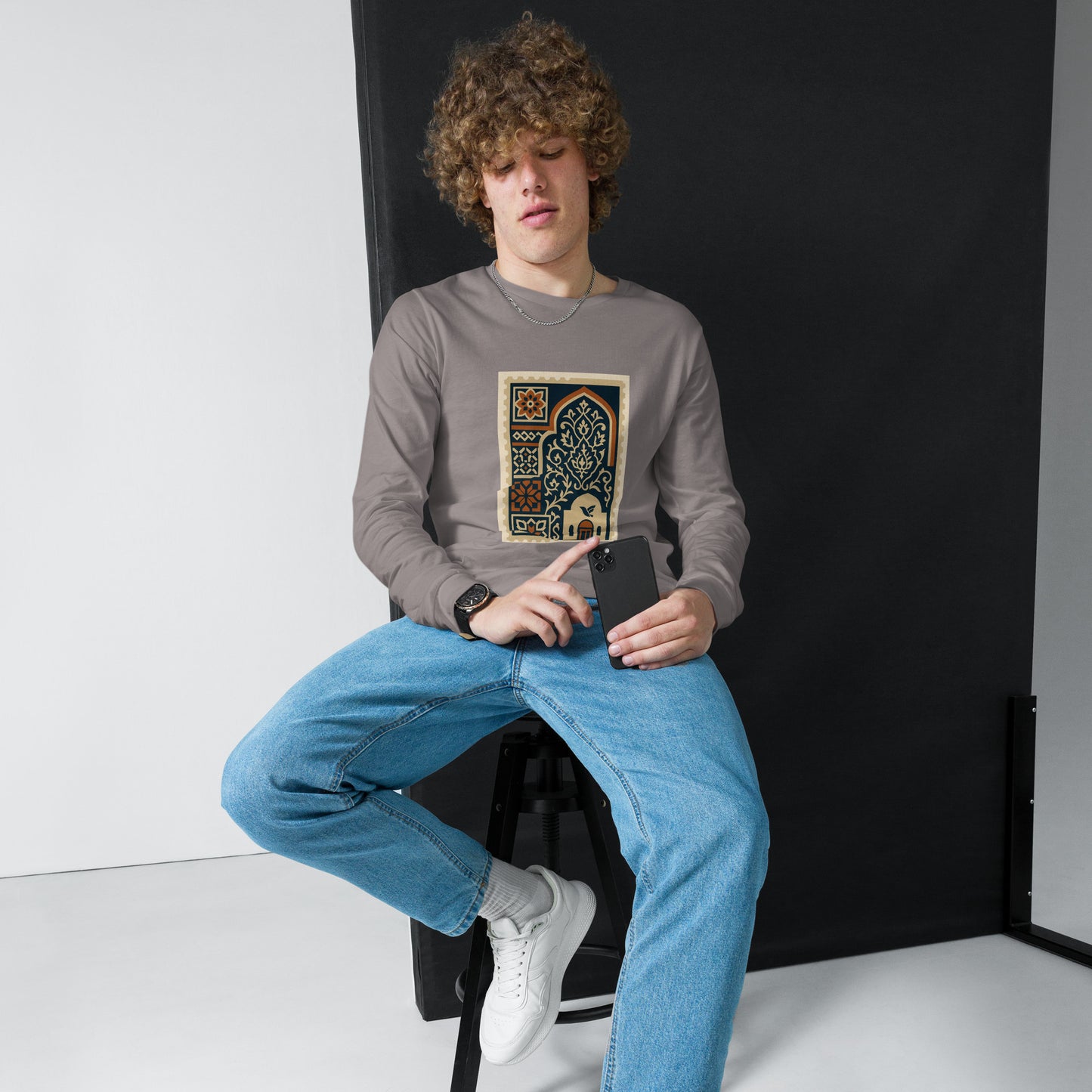 Person wearing a gray sweatshirt with a colorful design, sitting on a black stool against a white background.