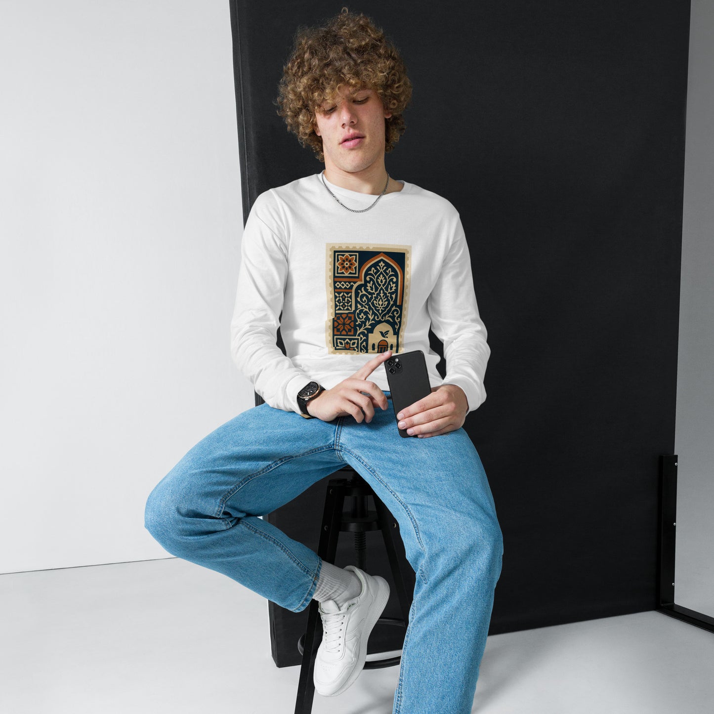 Person wearing a white sweatshirt with a colorful graphic design, sitting against a black backdrop.